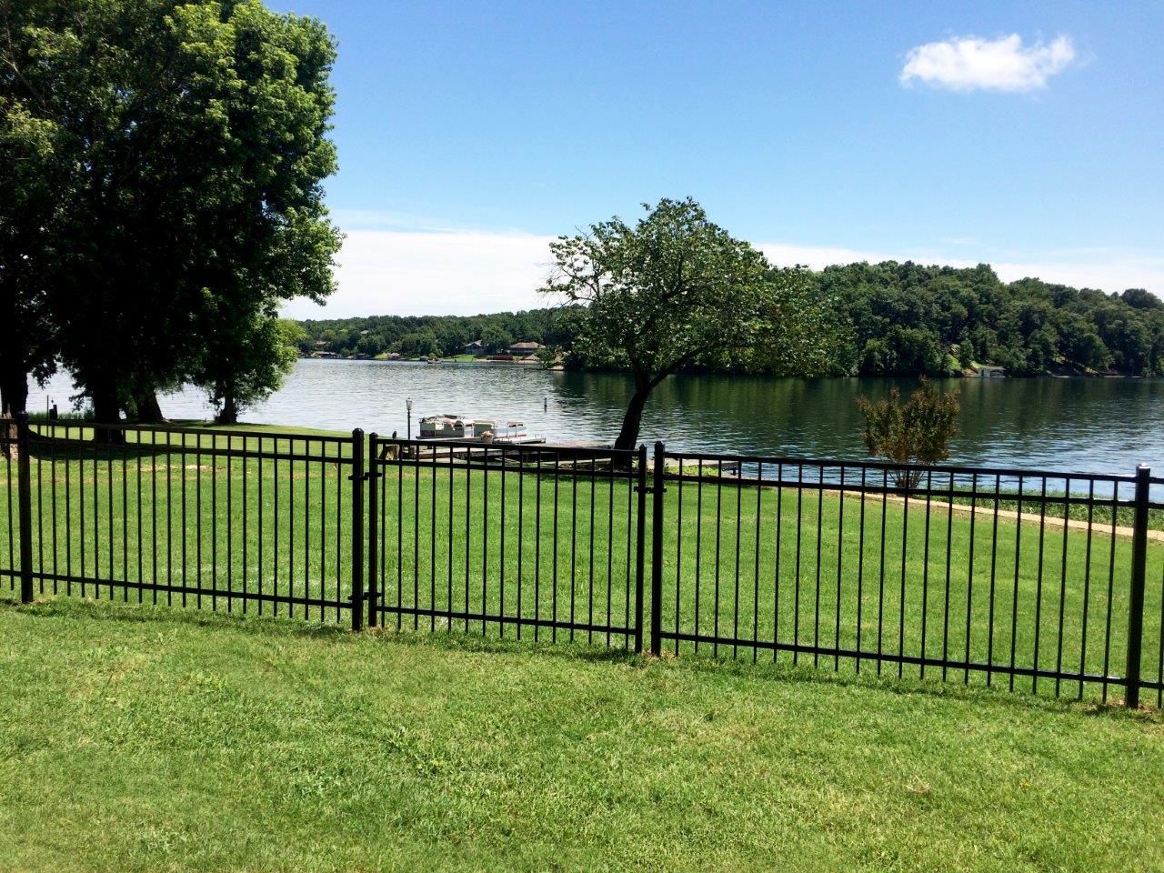 A black fence surrounds a lush green field with a lake in the background.