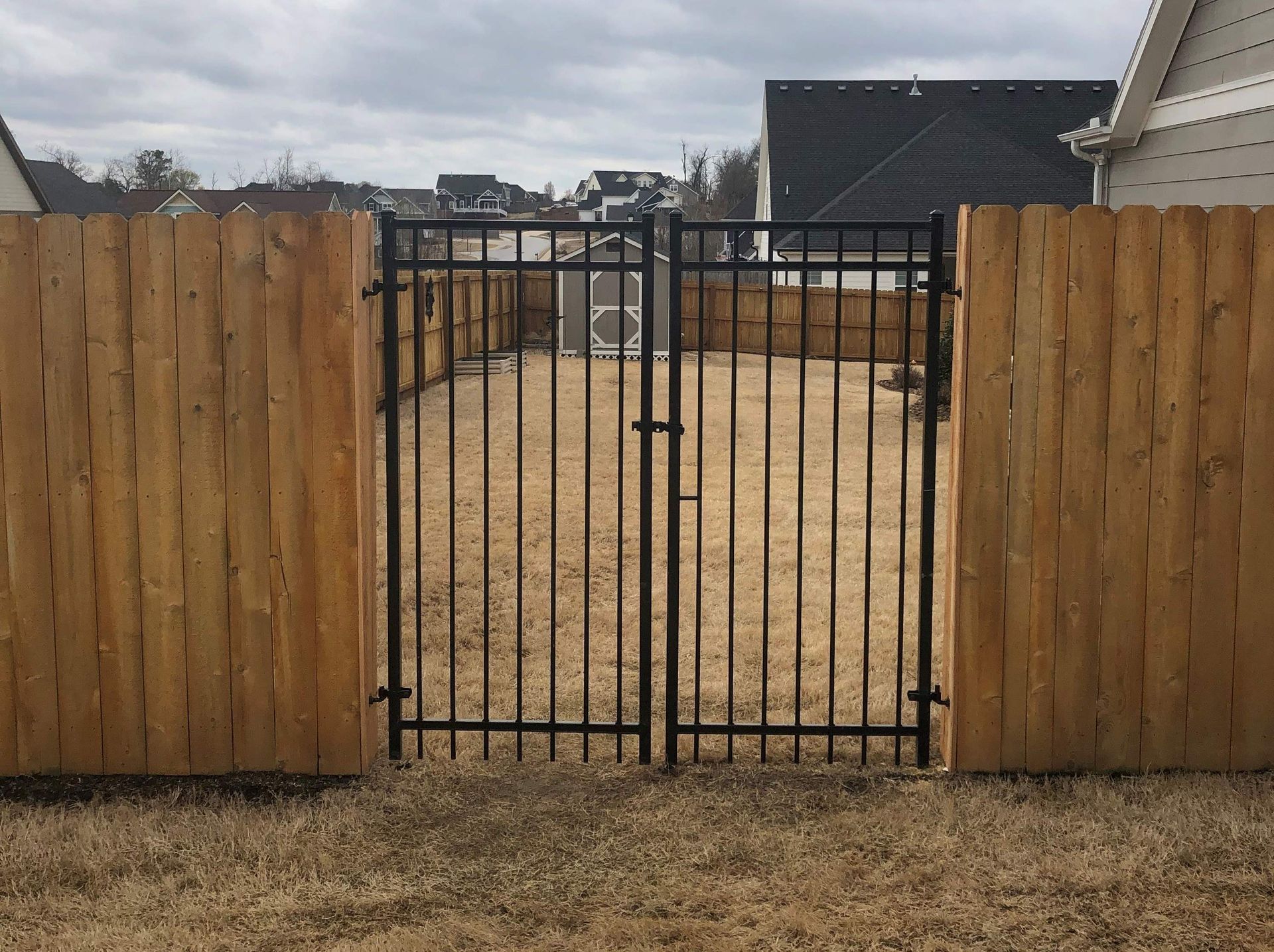 A wooden fence with a metal gate leading to a yard.