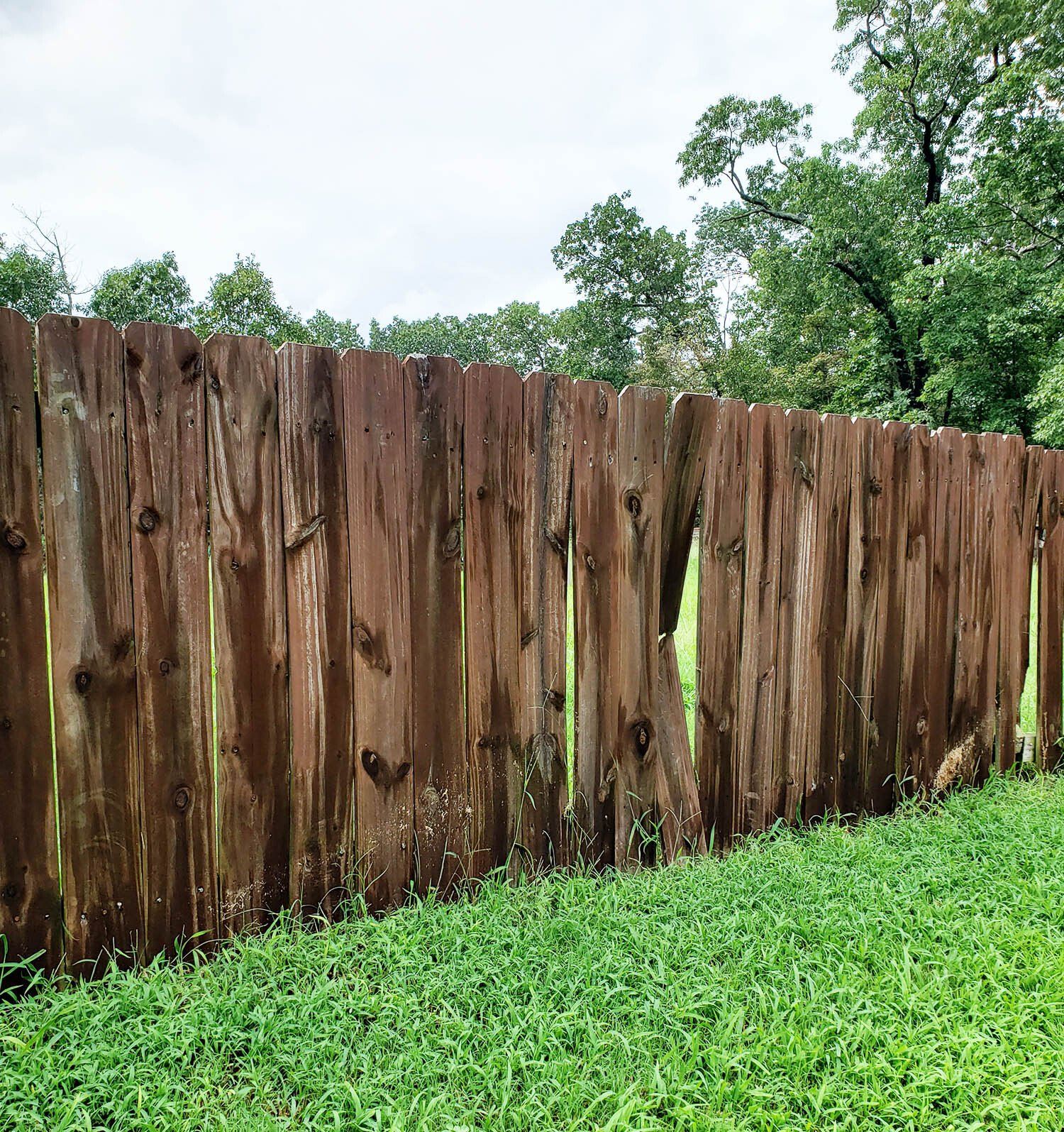 a broken wooden fence is surrounded by green grass and trees