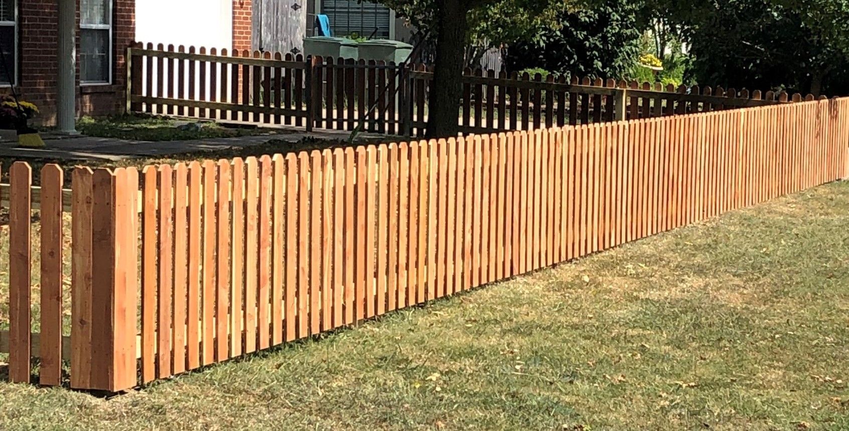 A wooden picket fence is sitting on top of a lush green lawn.
