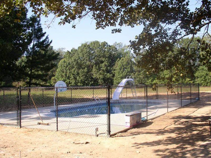 A swimming pool behind a chain link fence with trees in the background