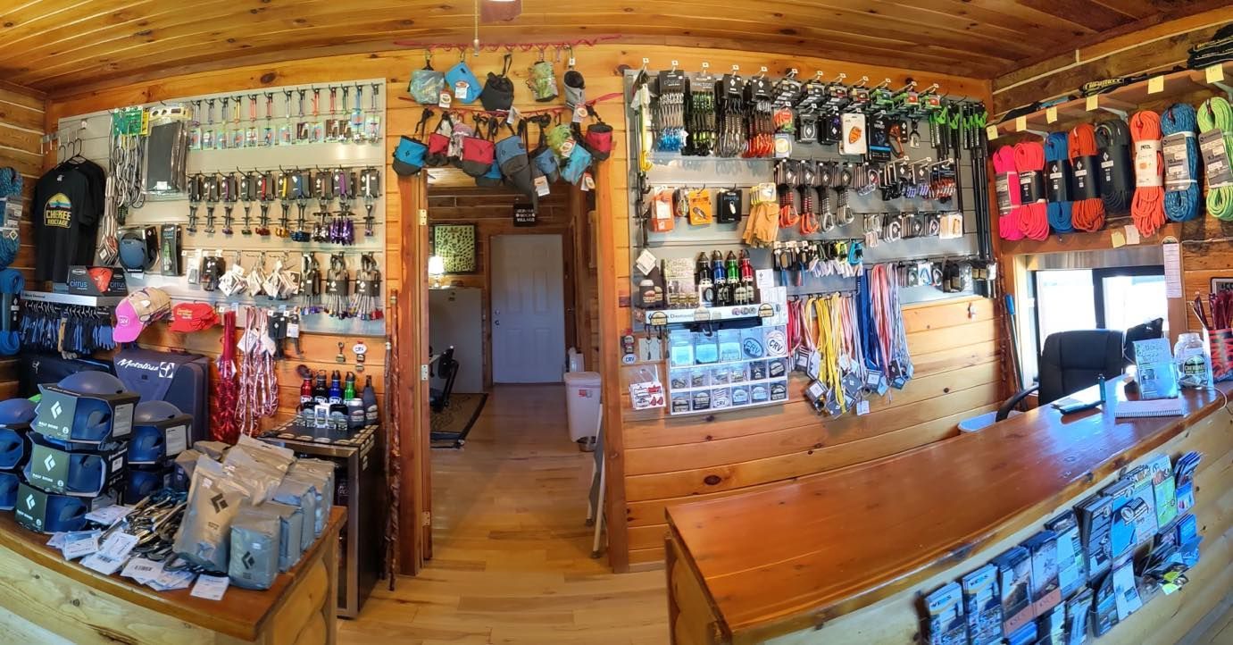 Inside a gear shop: shelves of equipment, backpacks, snowboards, a wooden counter, and a doorway.