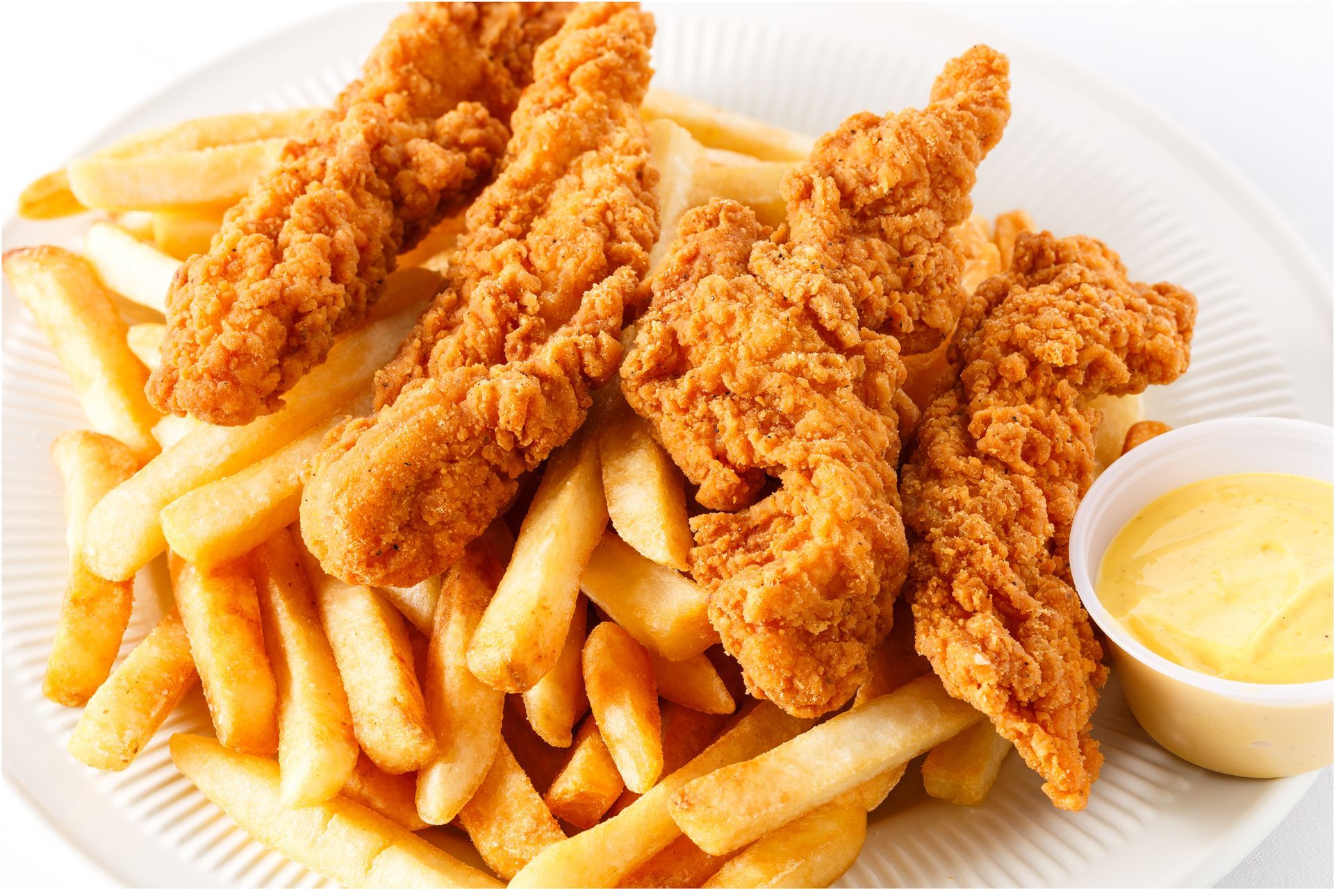 Chicken tenders and fries with dipping sauce on a white plate.