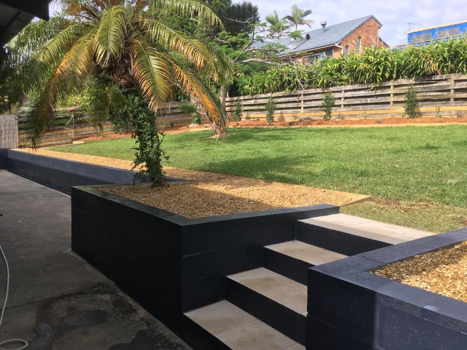 A Backyard Scene with A Dark, Tiered Retaining Wall — Creative Landscapes Coffs Harbour in Bellingen, NSW