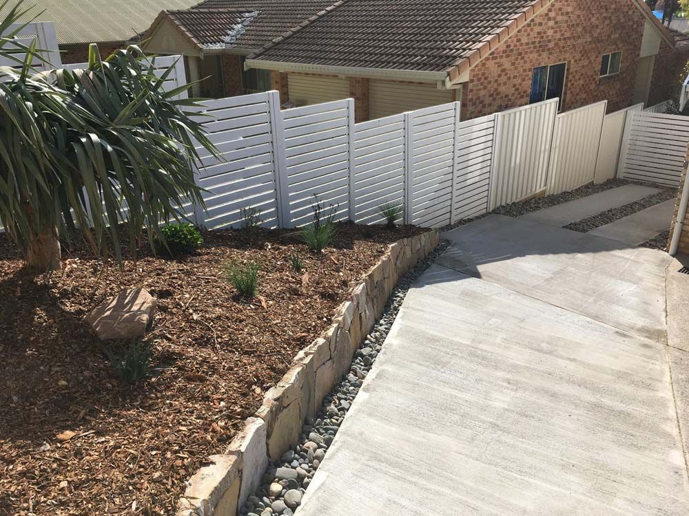 A Sloped Concrete Driveway Lined with A Stone Retaining Wall — Creative Landscapes Coffs Harbour in Korora, NSW
