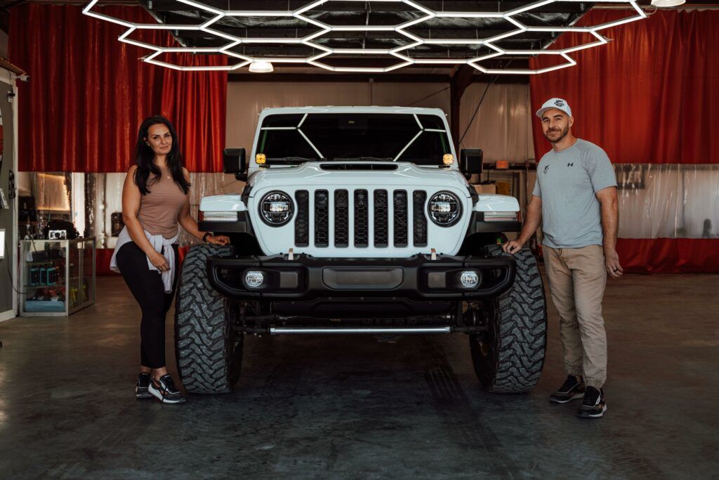 A white jeep with gold wheels is parked in a garage.