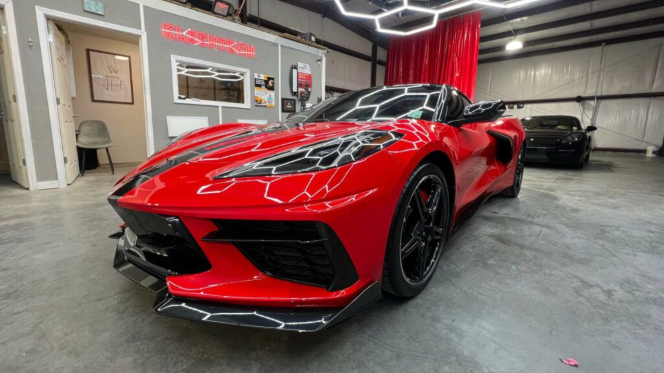 Red sports car in a modern garage with bright overhead lighting and gray concrete floor