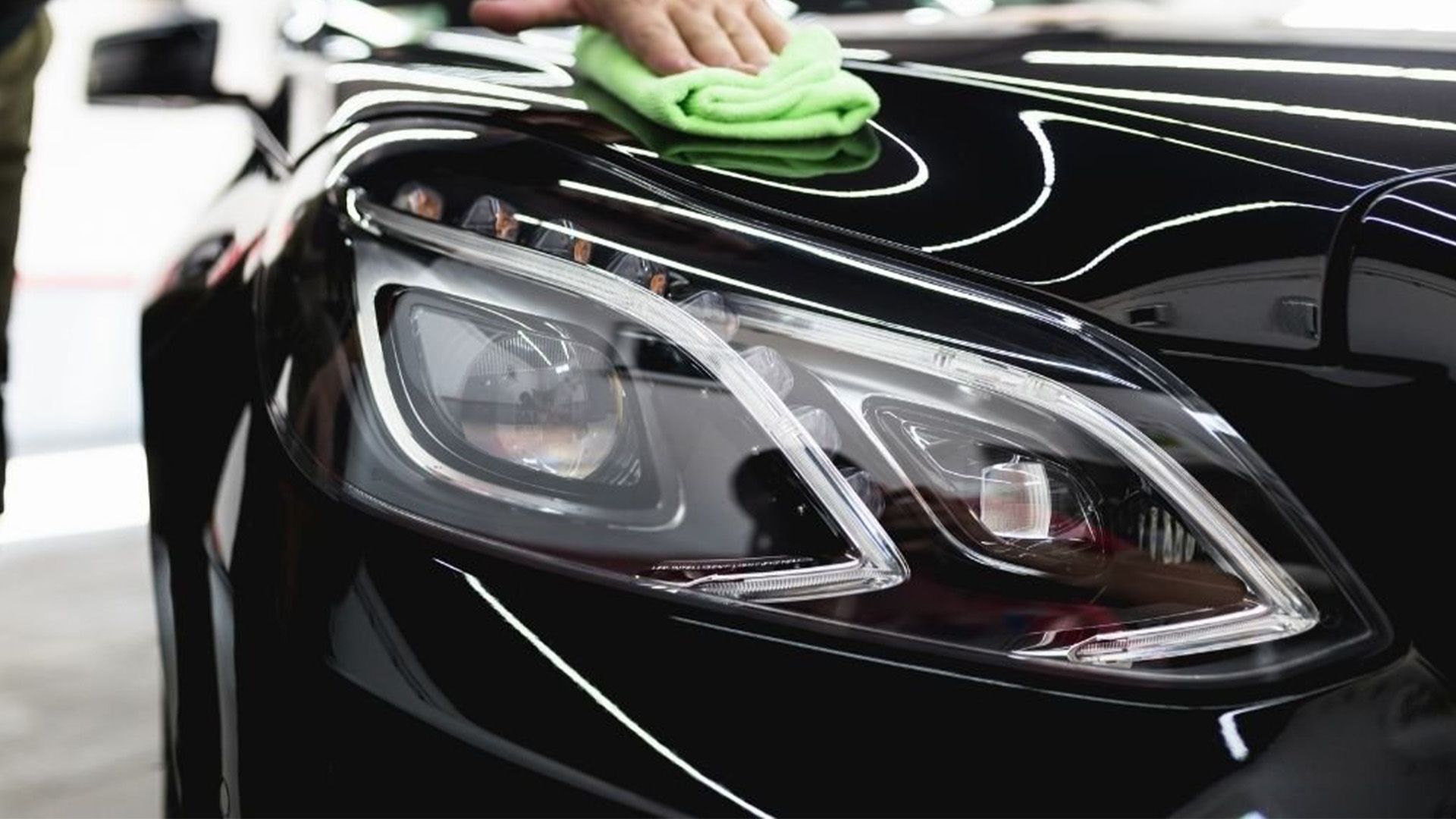 A person is cleaning a black car with a green cloth.