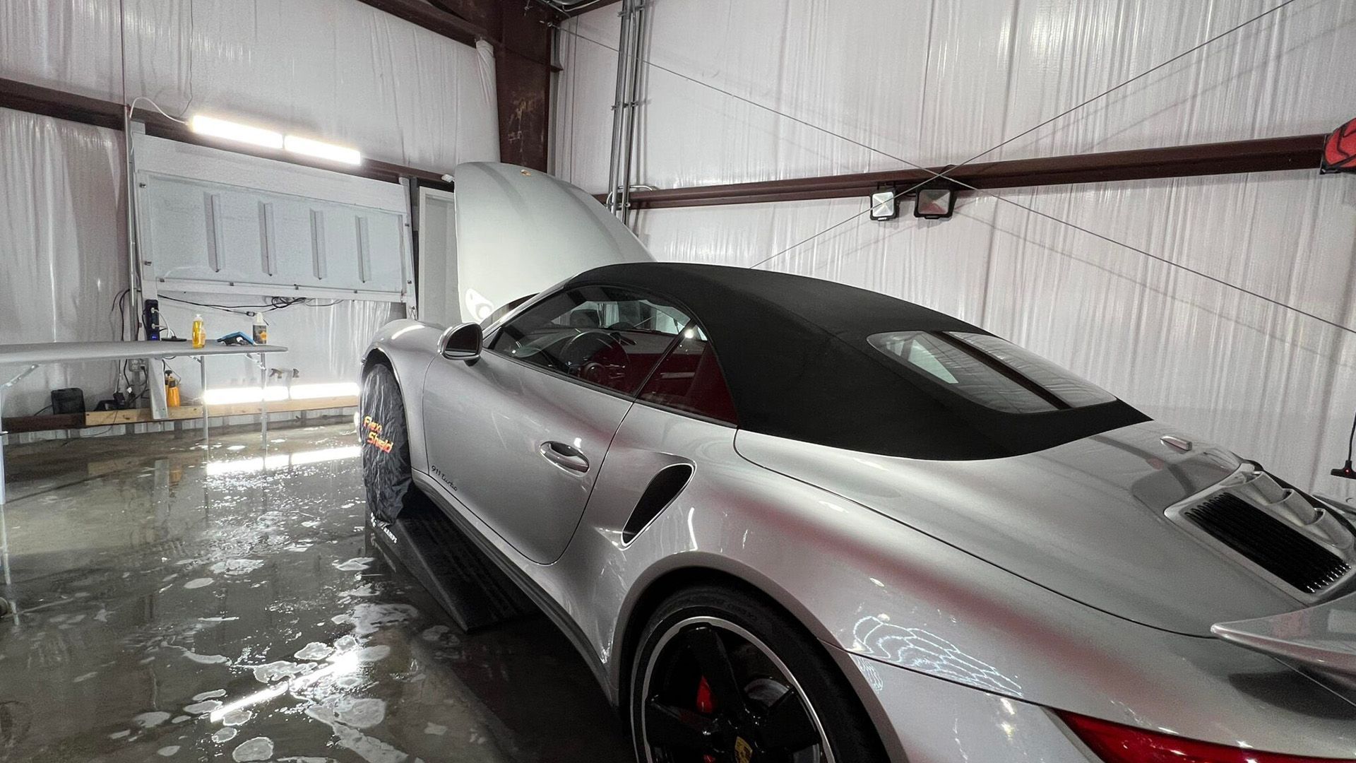 Silver sports car in a wet garage with an open door and bright overhead lighting