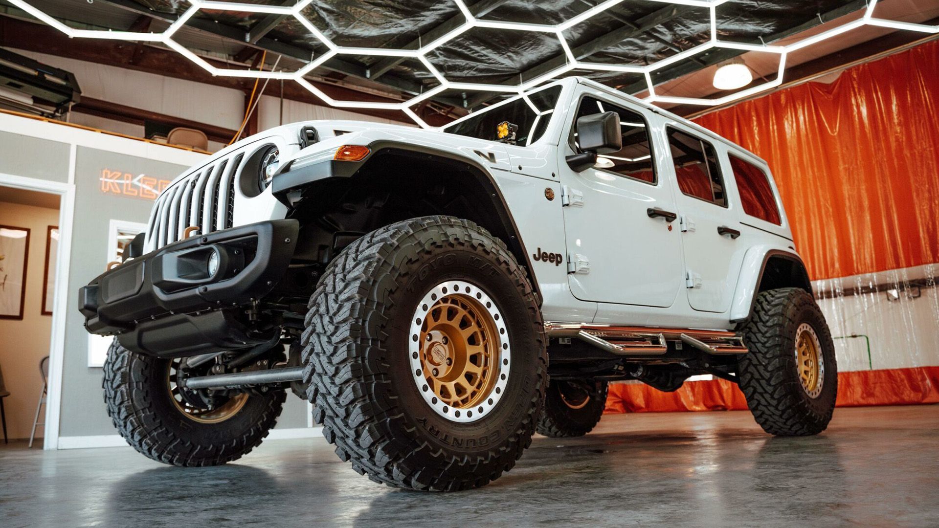 A white jeep with gold wheels is parked in a garage.