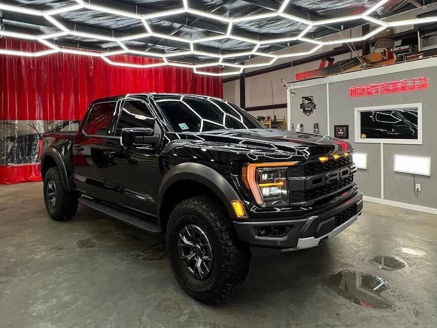 Black lifted pickup truck in a showroom with red curtains and hexagonal ceiling lights