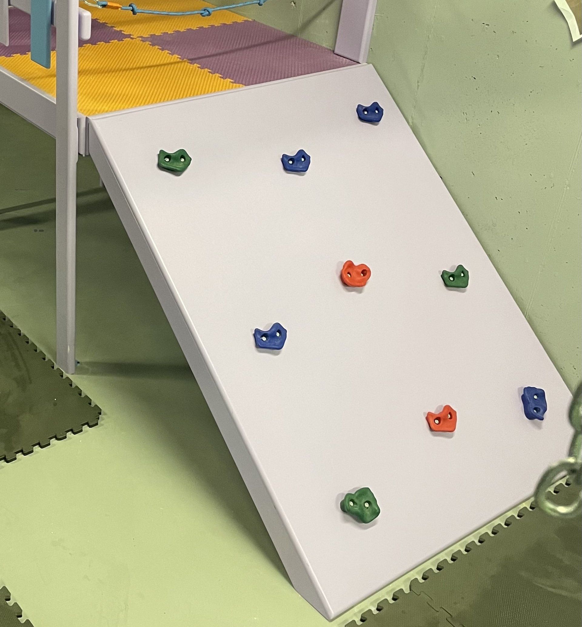 Custom angled sensory gym rock wall with colorful climbing holds, padded flooring, and elevated platform