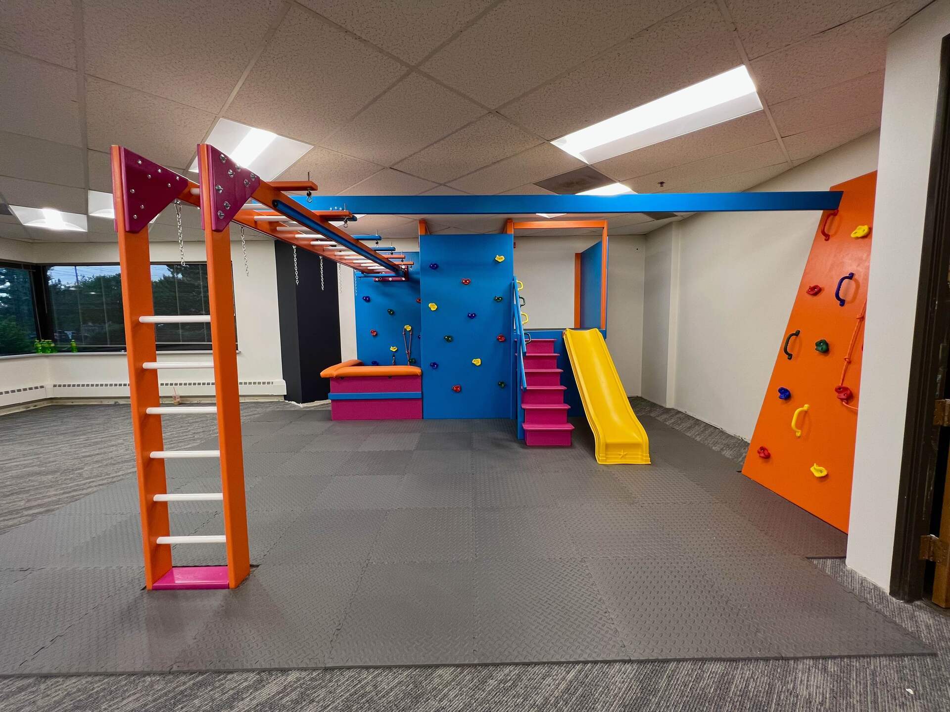 Commercial sensory gym with climbing wall, ladder, slide, and colorful padded activity area
