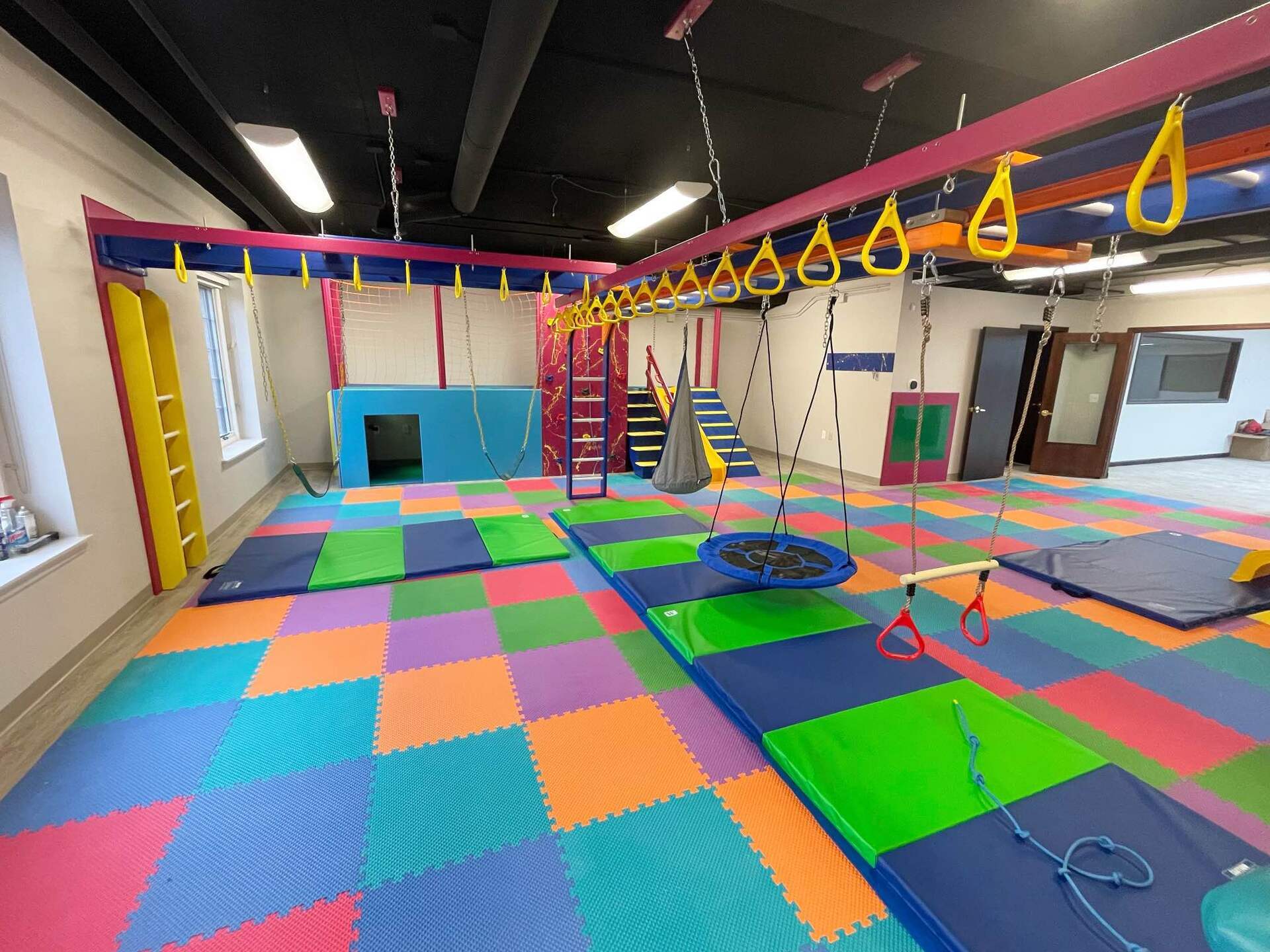 Commercial sensory gym with monkey bars, overhead rings, padded flooring, and colorful movement equipment
