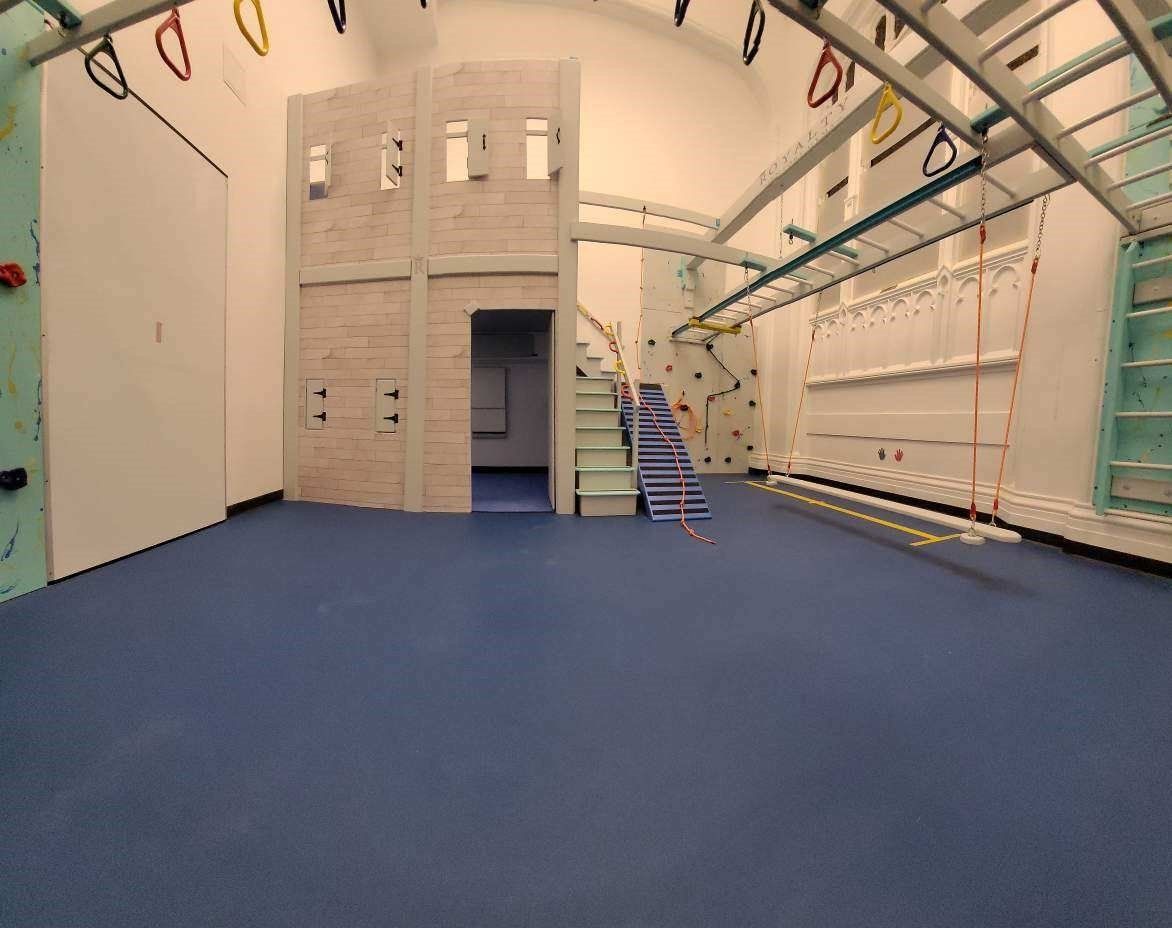 Commercial sensory gym with climbing structure, overhead bars, padded flooring, and indoor therapy equipment