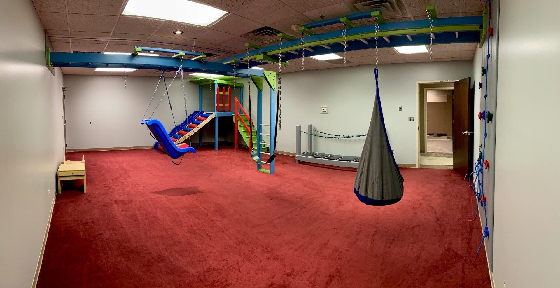 Commercial sensory gym with swing, climbing structure, padded flooring, and movement-based therapy equipment