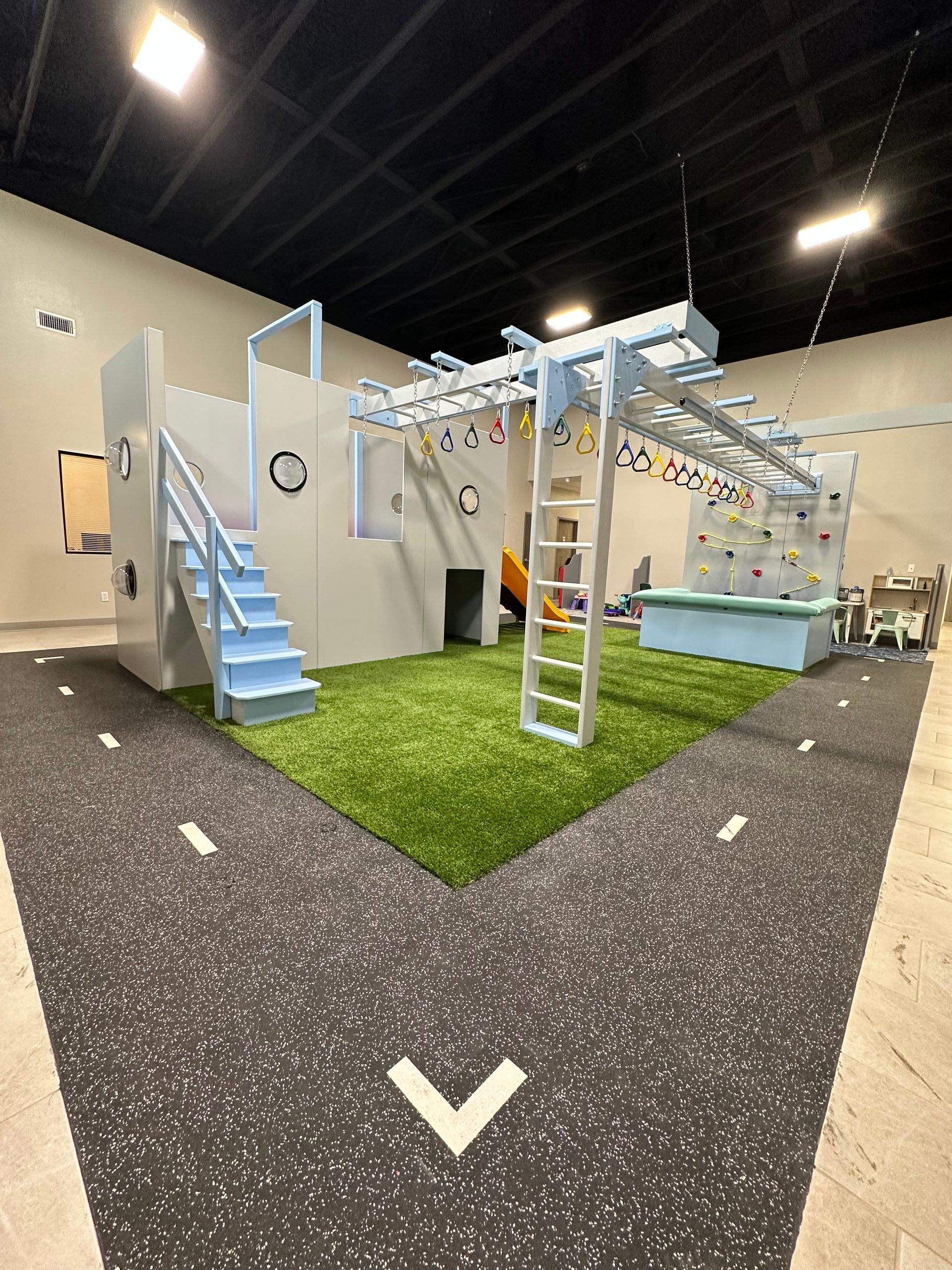 Commercial sensory gym with castle-style climbing structure, ladder, overhead bars, and padded flooring
