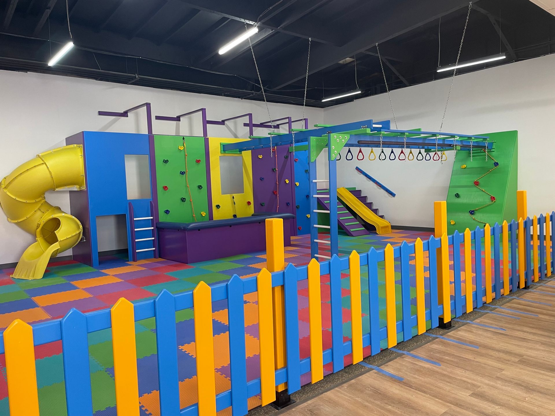 Commercial sensory gym with colorful play structure, climbing walls, padded flooring, and safety railing