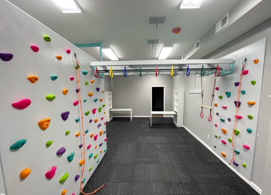 Sensory room with colorful rock climbing walls, padded flooring, and indoor movement play equipment