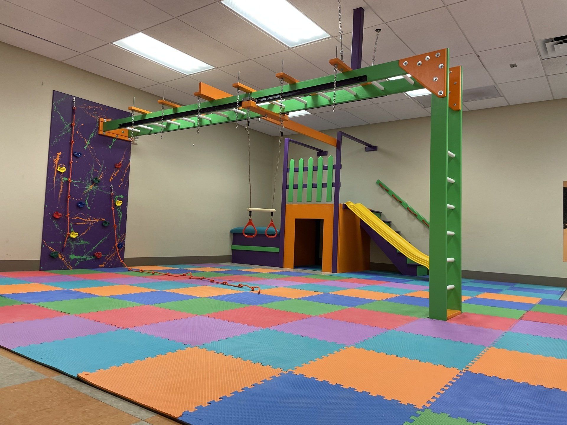 Commercial sensory gym with monkey bars, climbing wall, padded flooring, and colorful movement space
