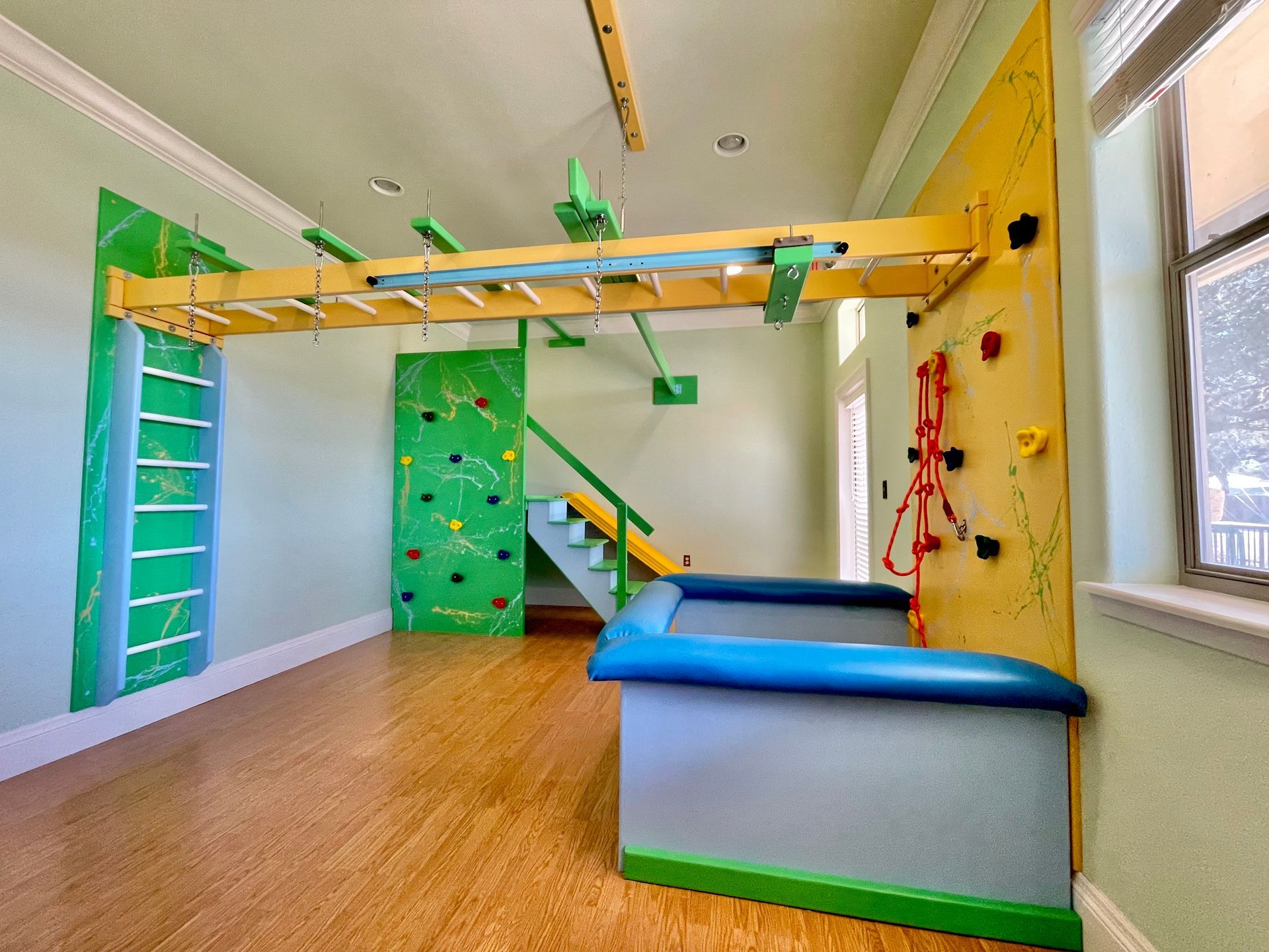 Custom home sensory gym with monkey bars, climbing wall, swing, and padded therapy equipment