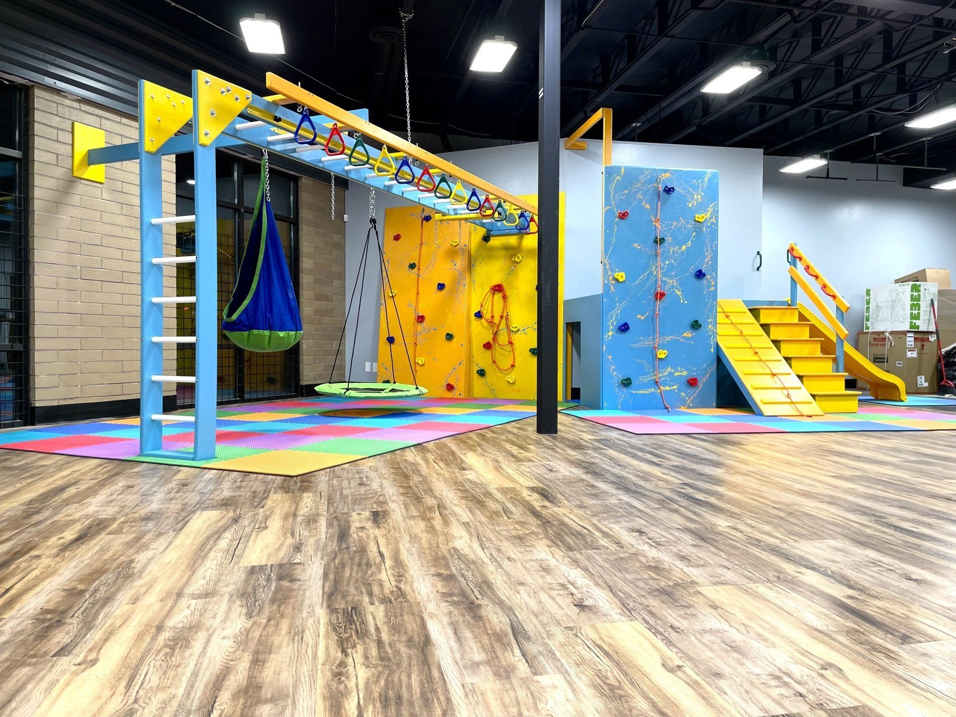 Commercial sensory gym monkey bar system with swing attachments and a padded crash pit