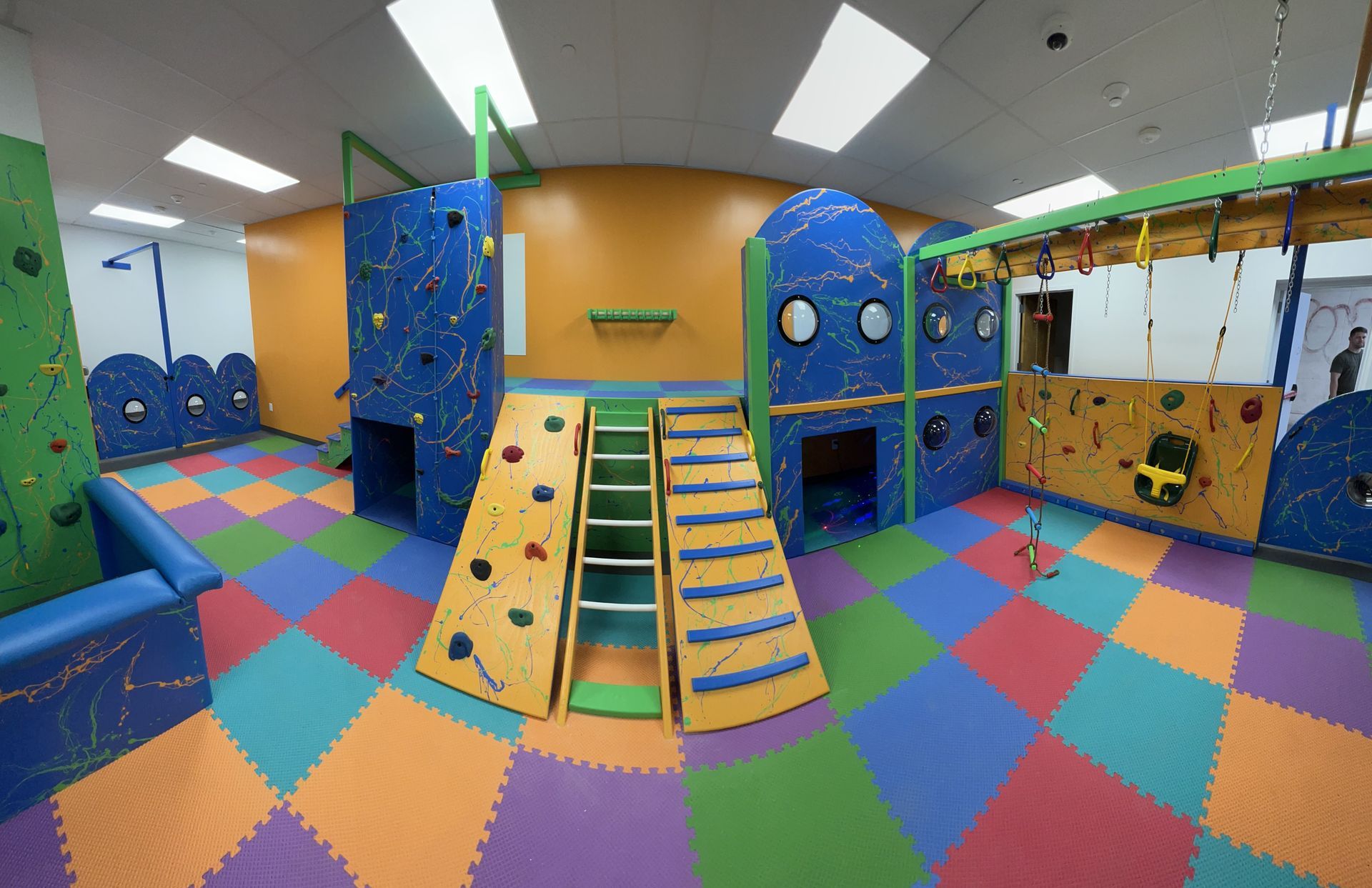Commercial sensory gym with climbing ramp, slide, activity walls, and colorful padded floor tiles