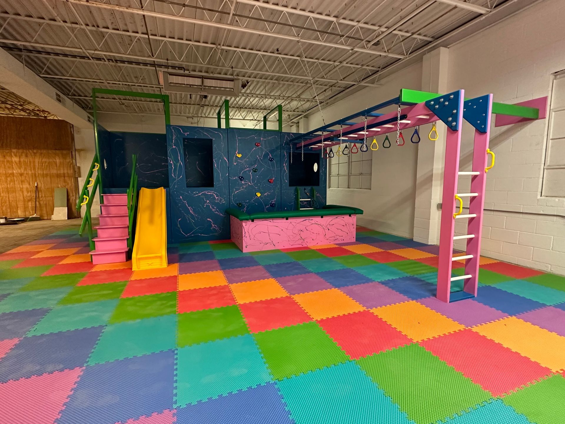 Commercial sensory gym with slide, climbing structure, overhead equipment, and colorful padded flooring