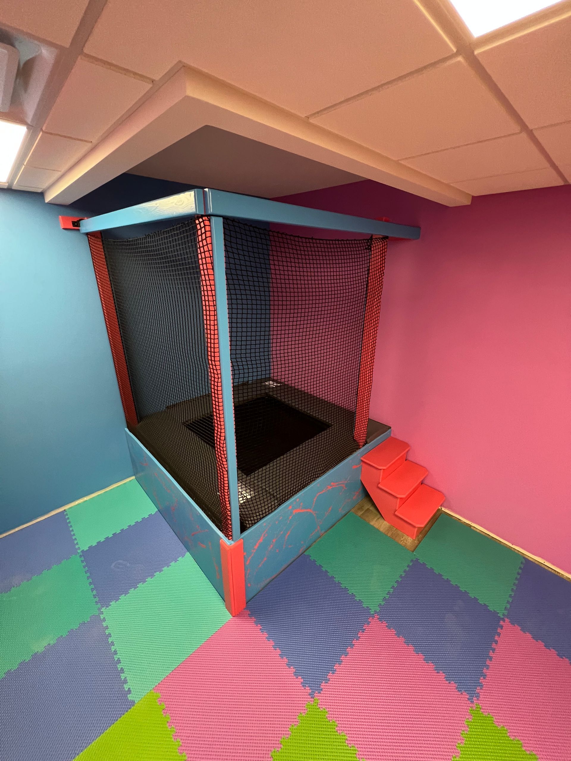 Sensory trampoline enclosure with protective netting, padded framing, and padded overhead surfaces