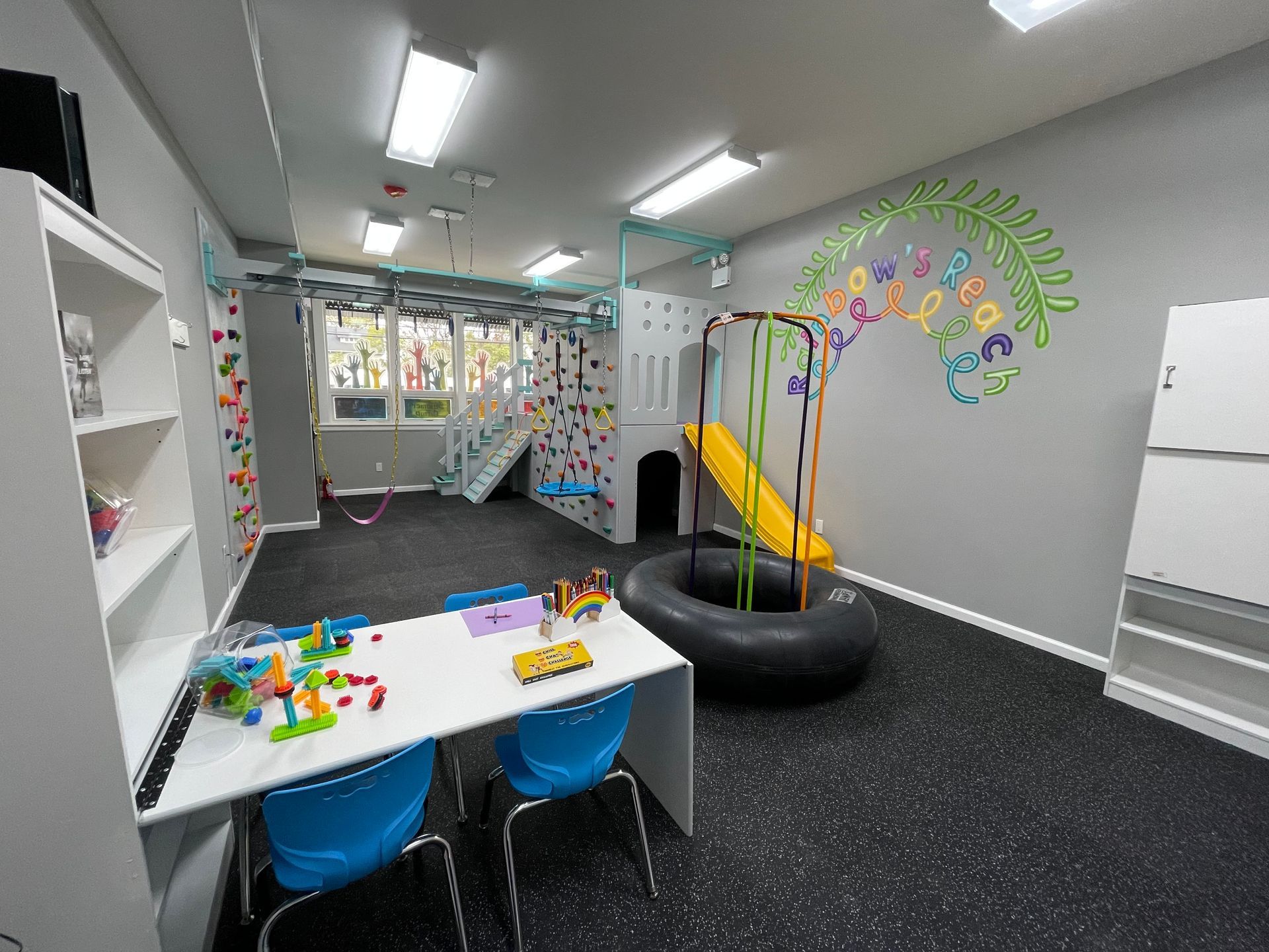 Commercial sensory gym with round platform swing, climbing wall, padded mats, and wall activity features