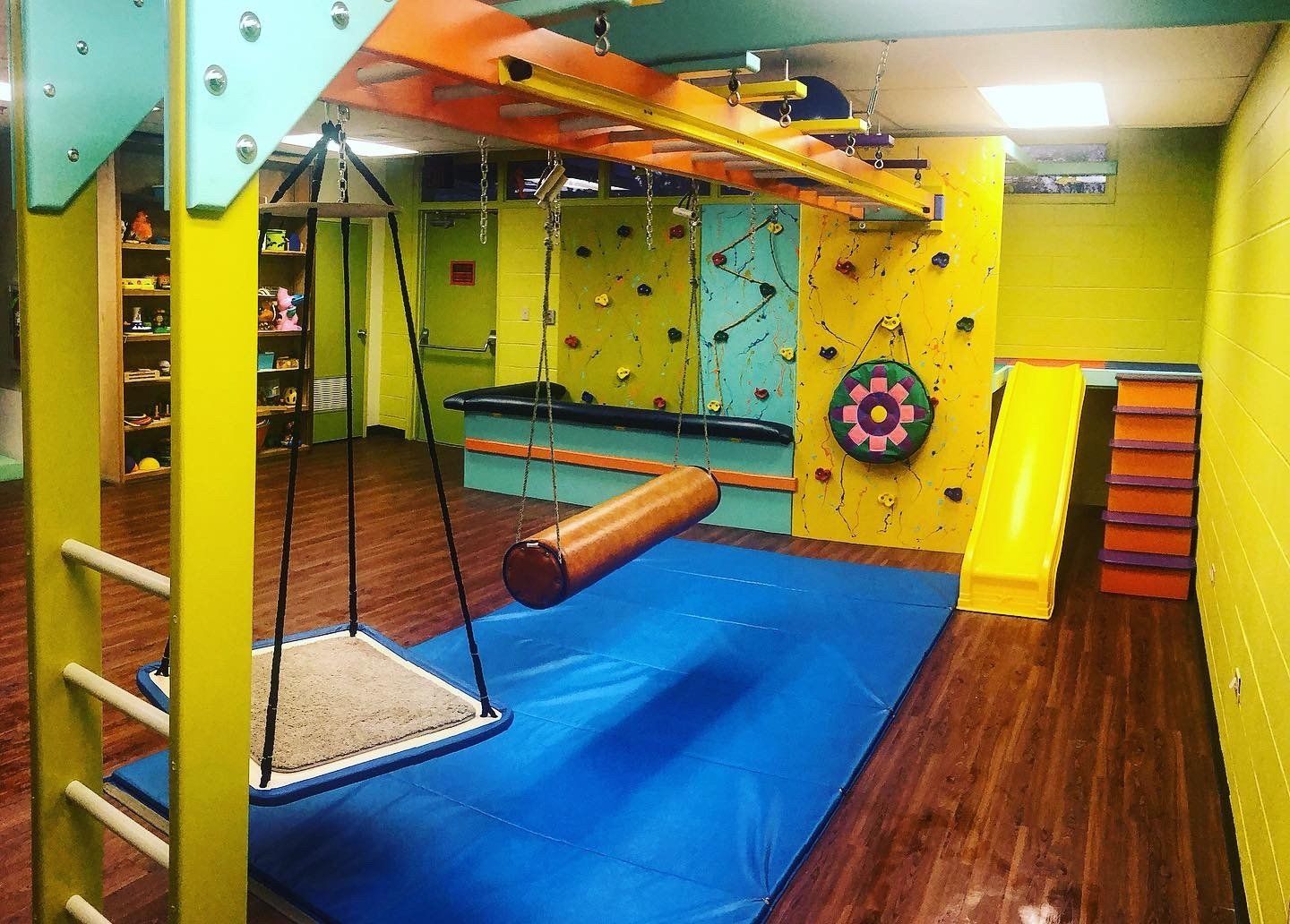 Custom sensory room with climbing wall, swing, padded flooring, and colorful therapy gym equipment