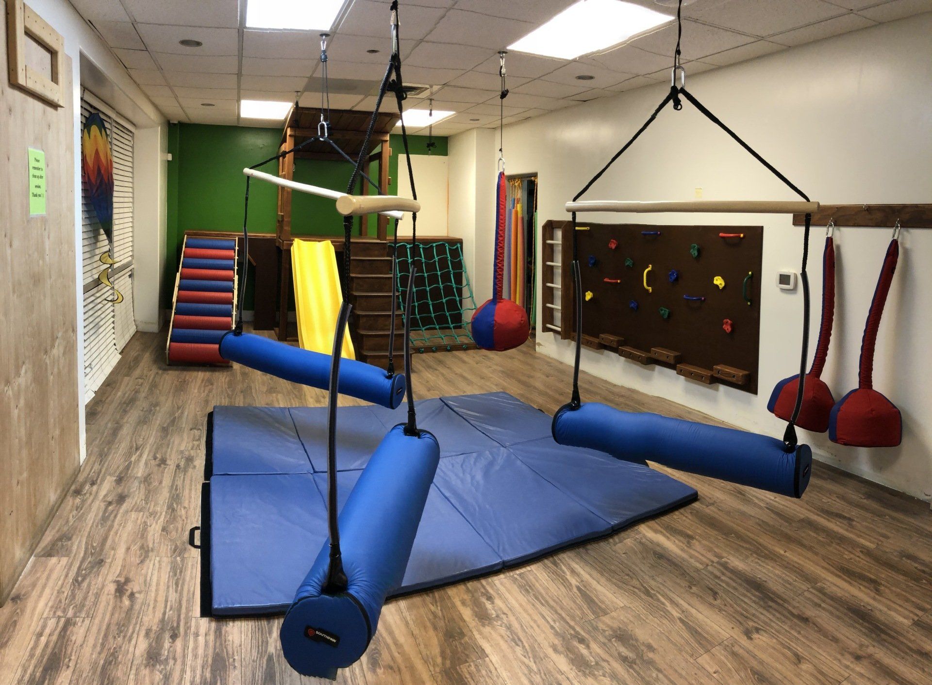 Therapy clinic sensory gym with platform swing, padded mats, climbing equipment, and activity walls