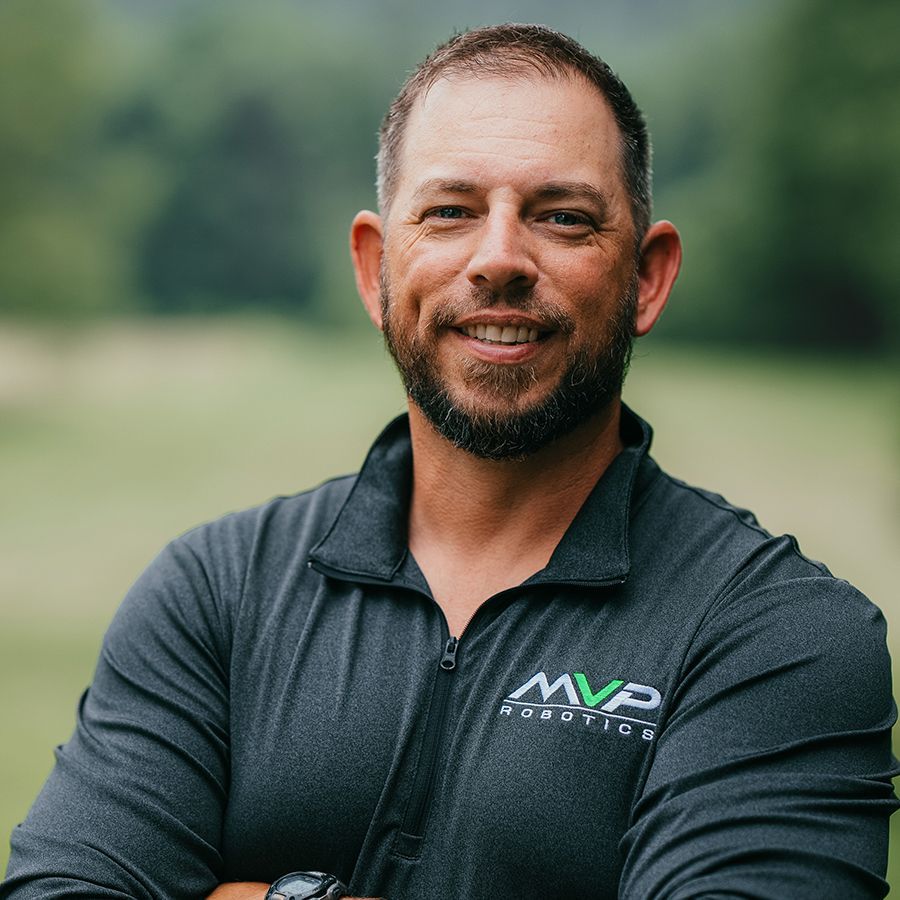Smiling person in a dark polo shirt standing outdoors with a blurred green background
