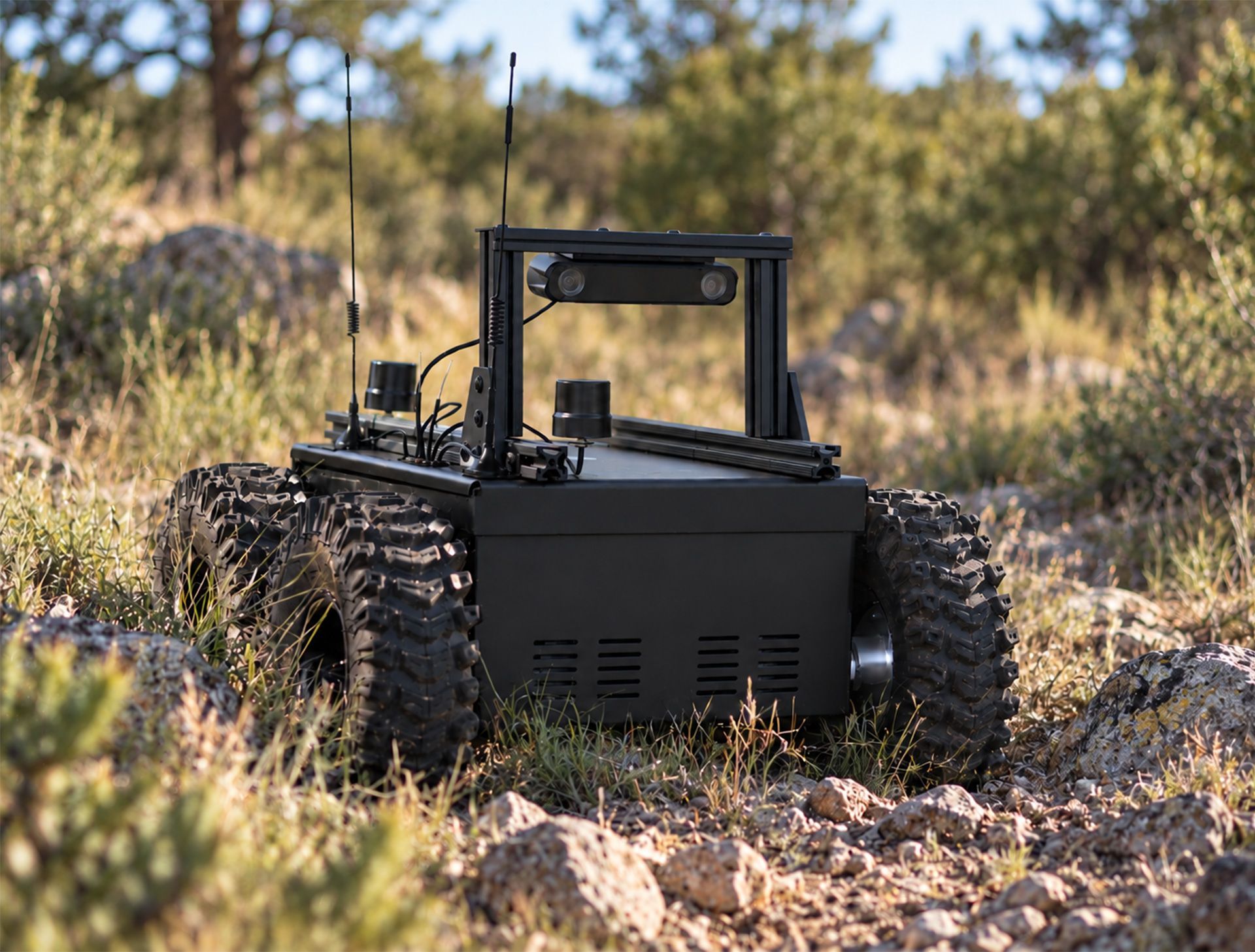 Black tracked robot rover on rocky ground in a dry grassy field