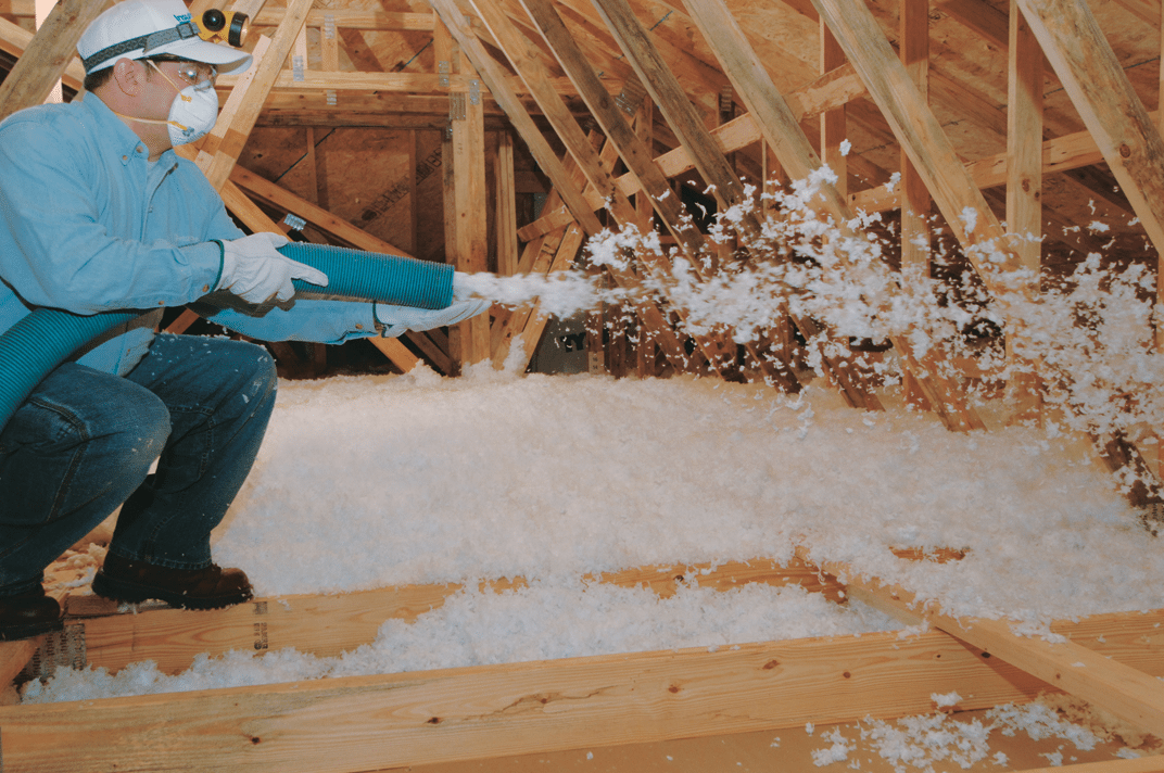 A man is blowing insulation into the attic of a house.