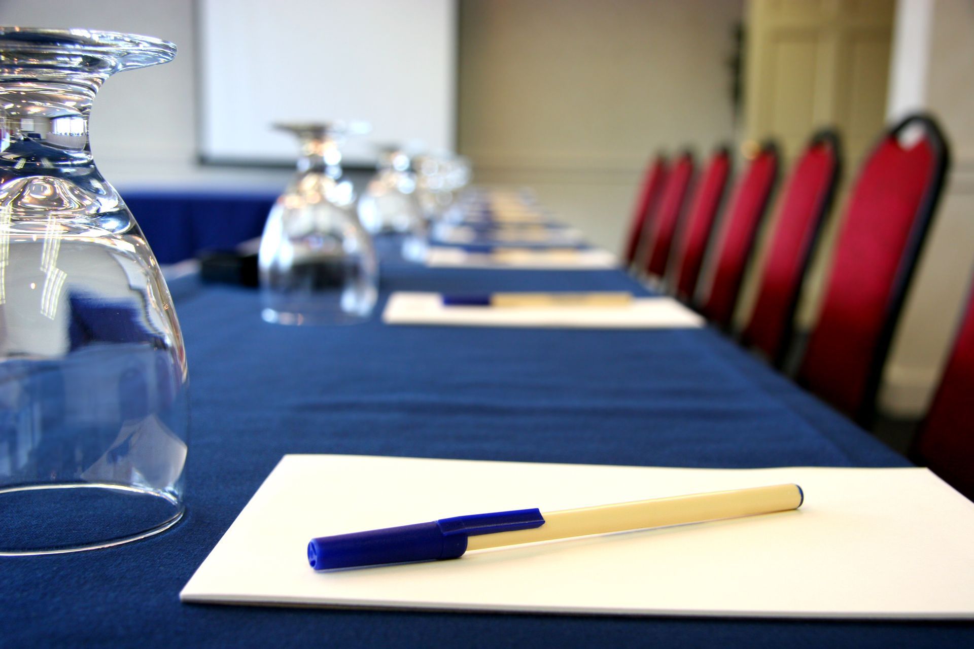 Conference table set with paper, pen, glasses, and red chairs, ready for a meeting.