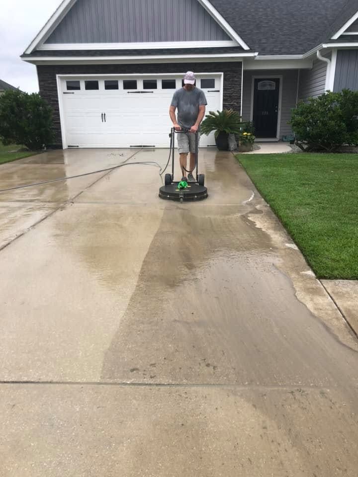 Person pressure-washing a wet driveway in front of a suburban garage