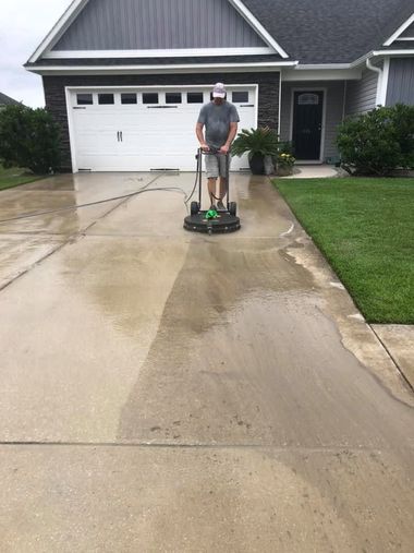 Person pressure-washing a wet driveway in front of a suburban garage