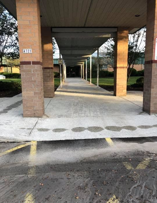 Covered outdoor walkway with brick columns, concrete path, and yellow parking lines leading into the distance