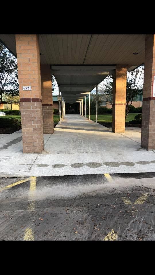 Covered outdoor walkway with brick columns, concrete path, and yellow parking lines leading into the distance