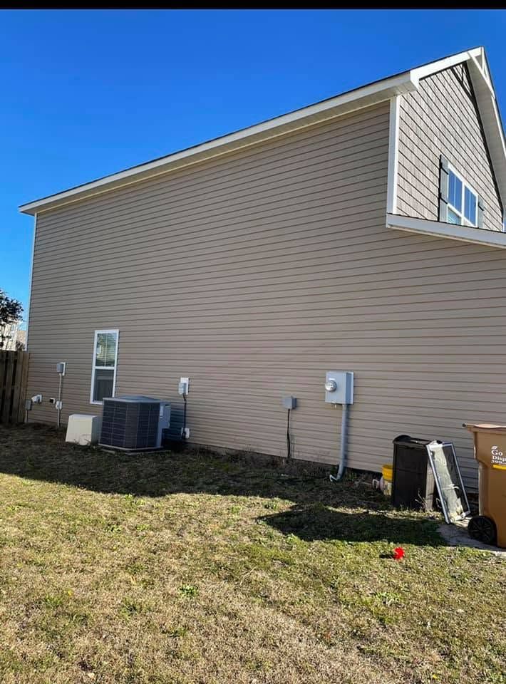 Side view of a beige house with vinyl siding, blue sky, and outdoor HVAC units on a grassy yard.
