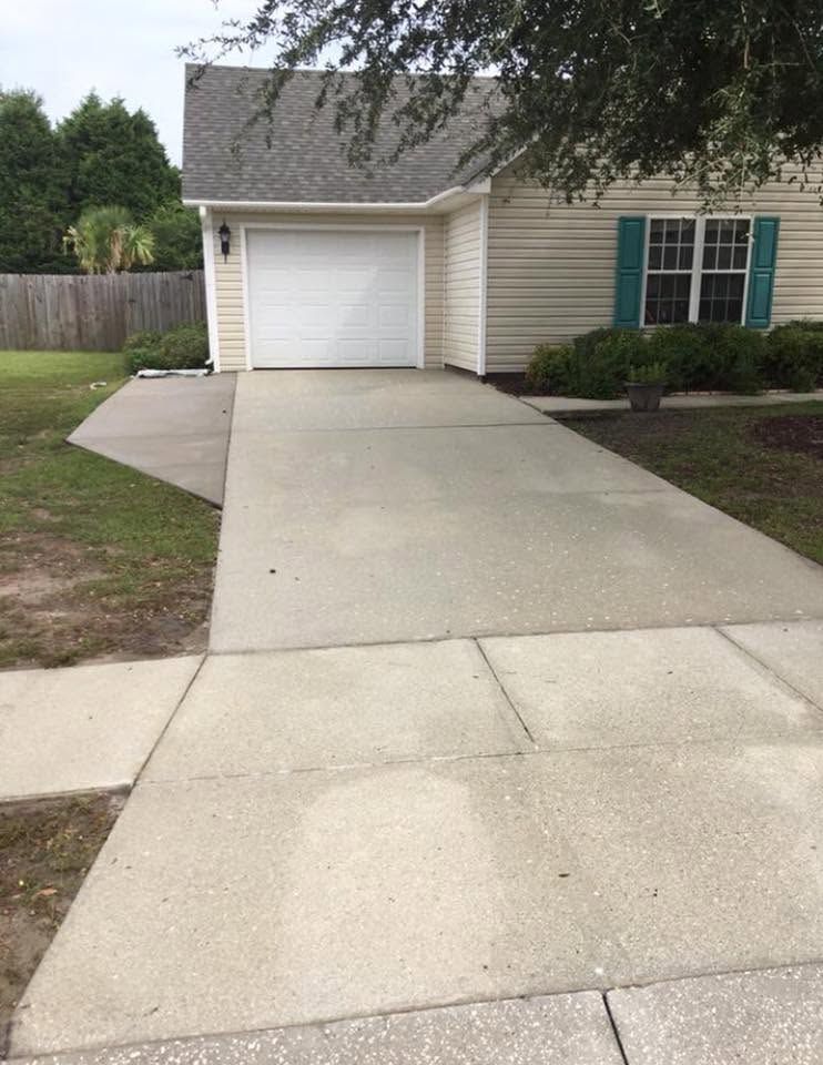 Concrete driveway leading to a white garage attached to a beige house with teal shutters.