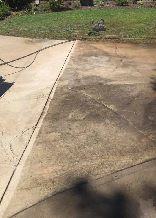 Cracked concrete driveway with a hose across it and a grassy front yard in the background