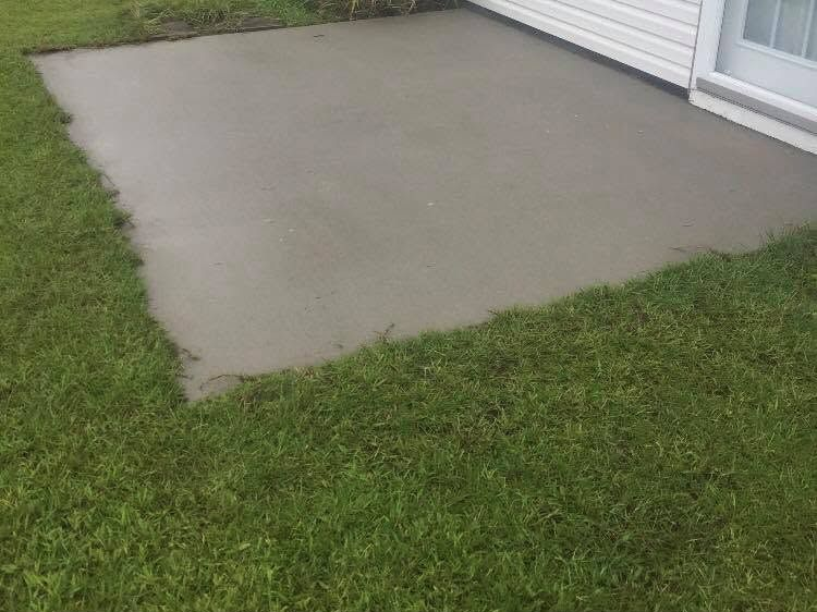 Concrete patio beside a white house, bordered by green grass