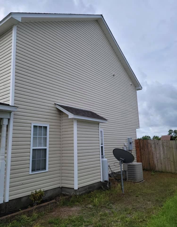 Side of a beige house with a small door awning, window, satellite dish, and fenced yard.