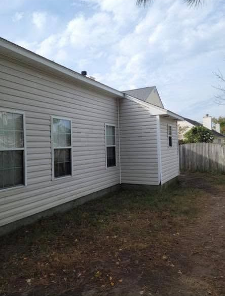 Side of a white house with windows, gravel yard, and a wooden fence under a cloudy sky