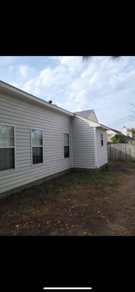 Side of a white house with windows, gravel yard, and a wooden fence under a cloudy sky