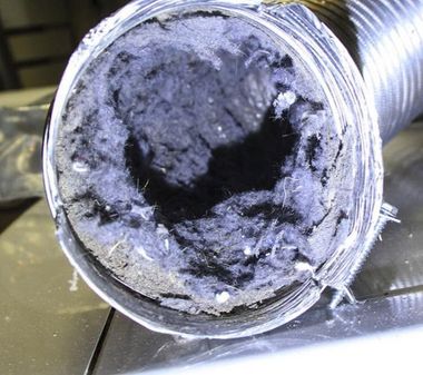Capped pipe end packed with gray lint and debris, showing a dark circular opening.