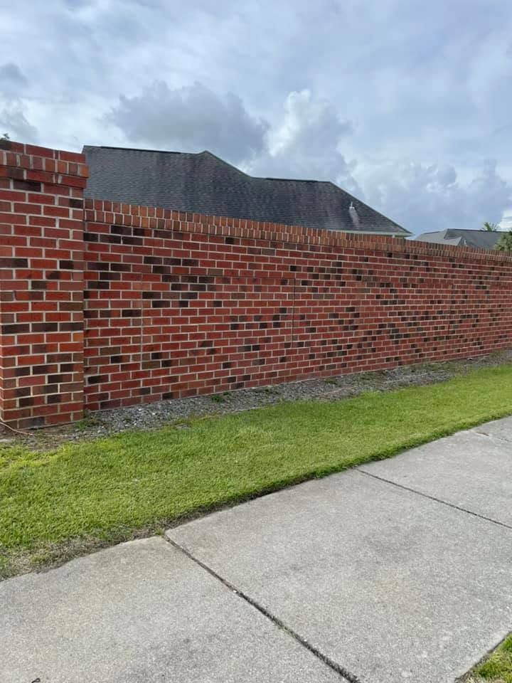 Long red brick wall beside a sidewalk and grass under a cloudy sky