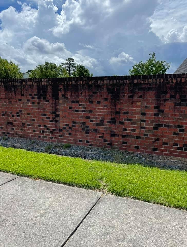 Red brick wall beside a sidewalk and bright green grass under a cloudy sky.